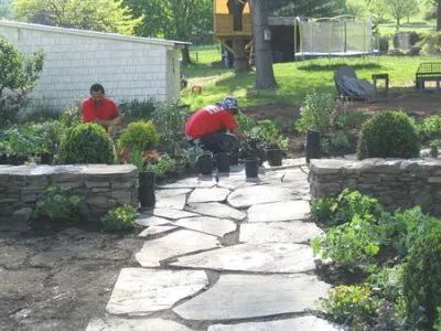 Two men are working on a stone walkway in a garden