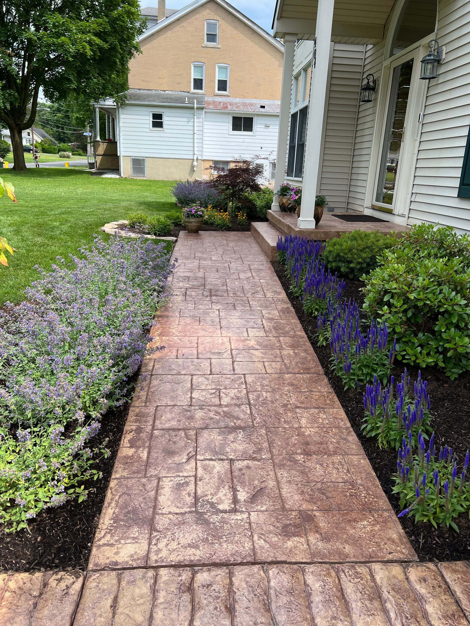 A brick walkway leading to a house surrounded by flowers and bushes.