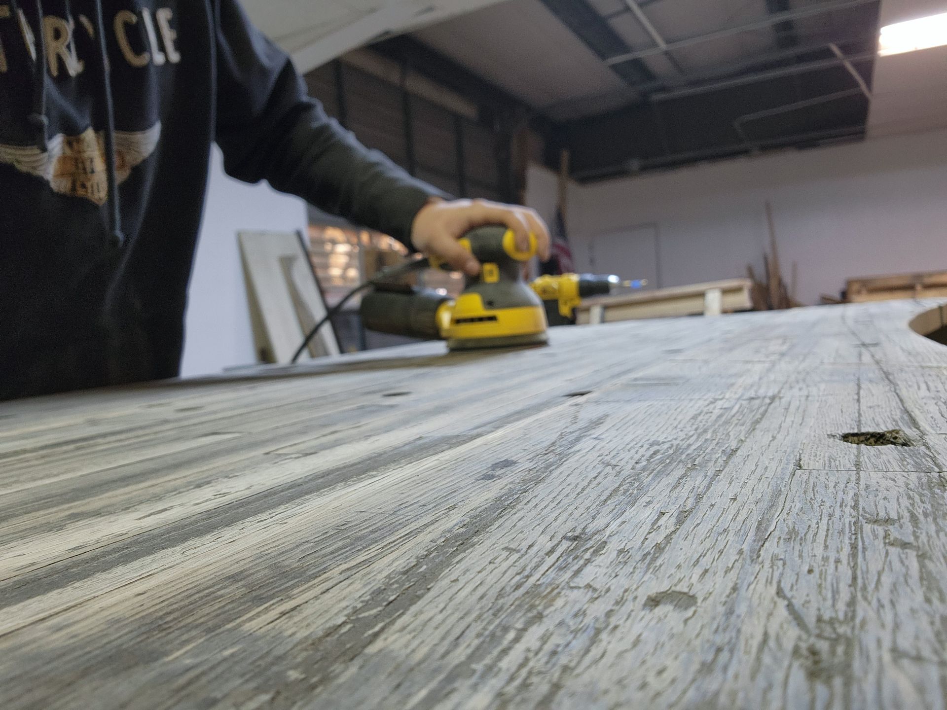 A person sanding a piece of wood with a yellow sander