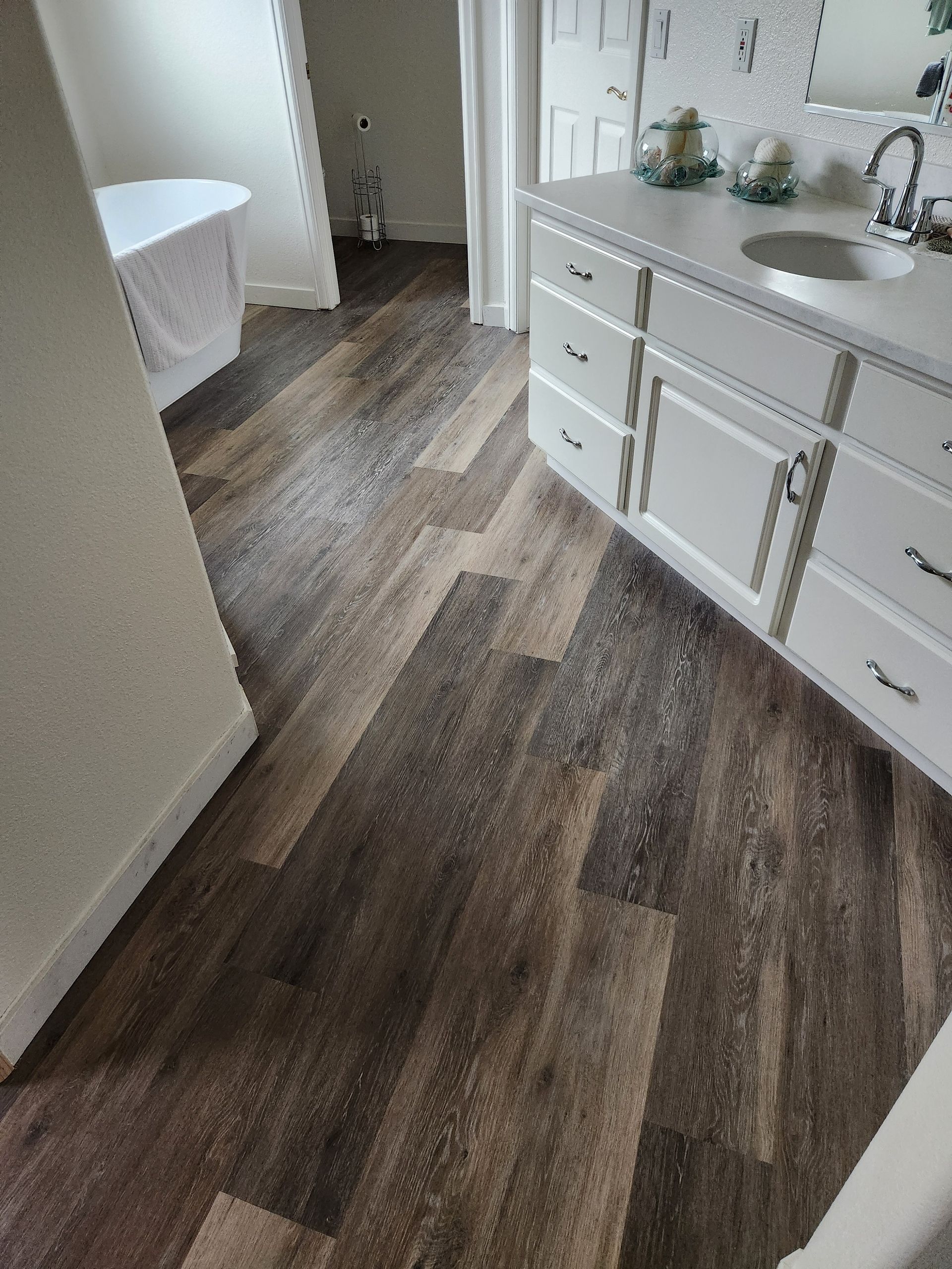 A bathroom with hardwood floors , white cabinets , a sink and a bathtub.