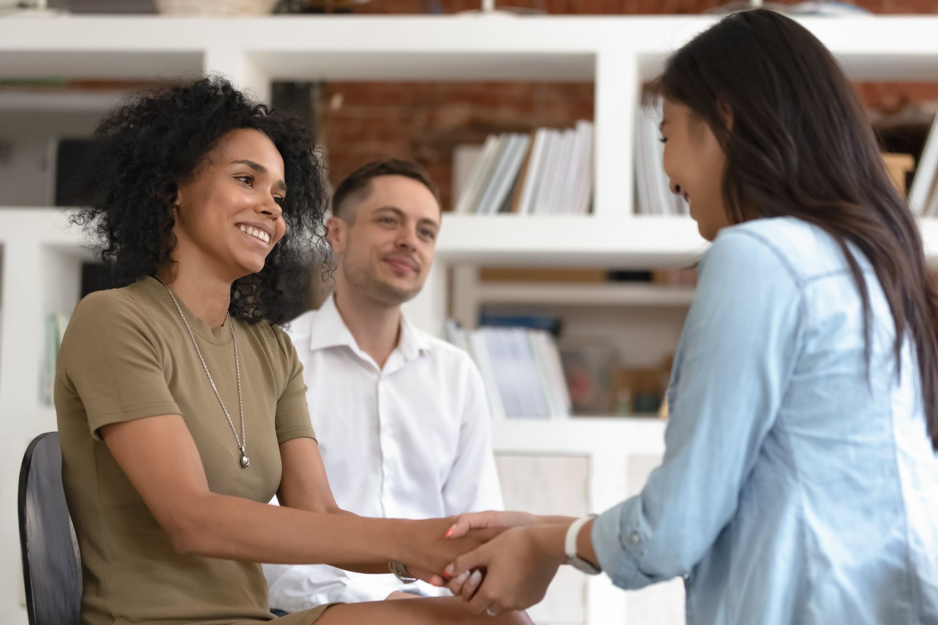 Three people shaking hands in a bright office, smiling during a meeting