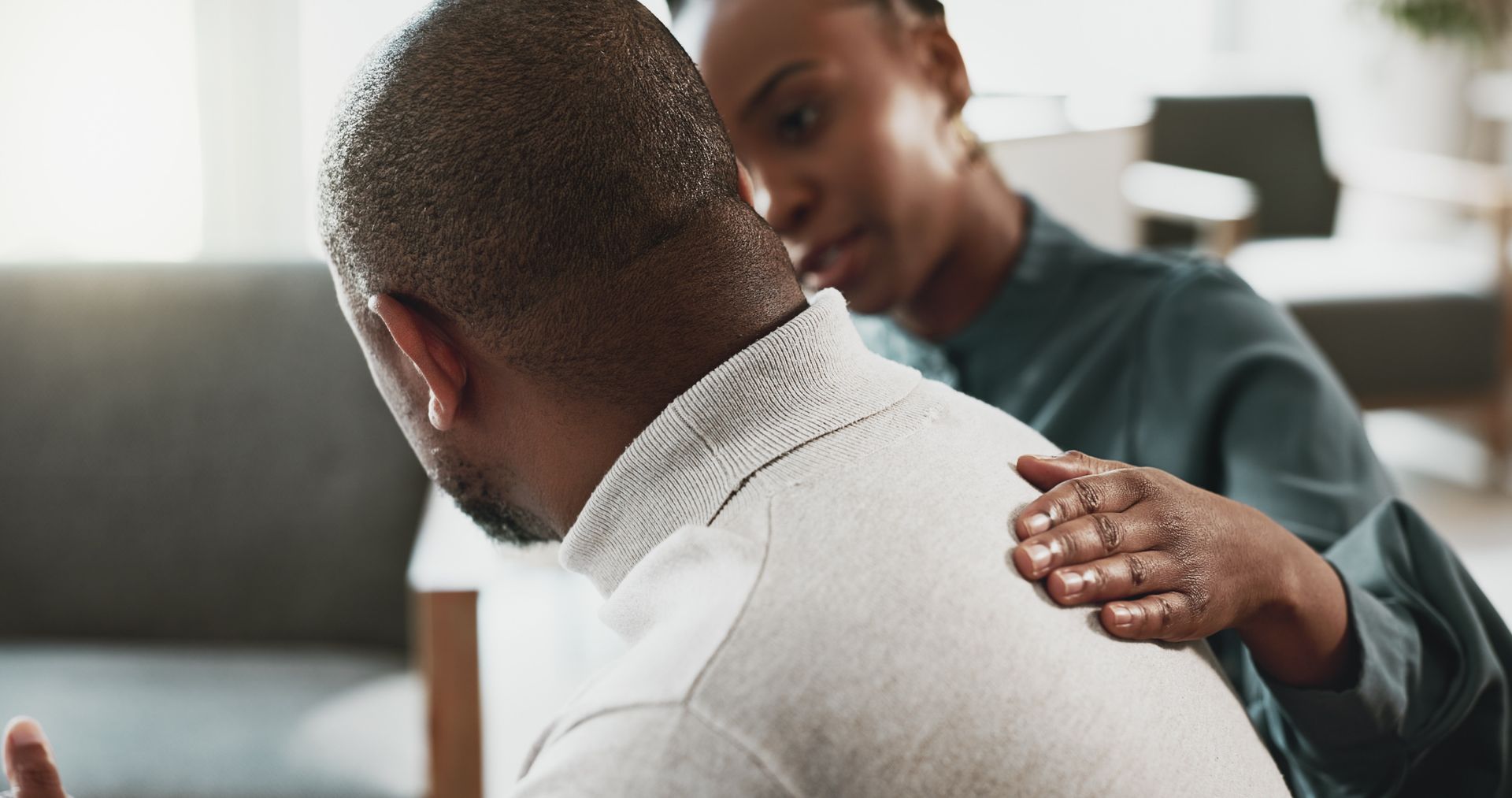 One person comforts another with a hand on their shoulder in an office setting.
