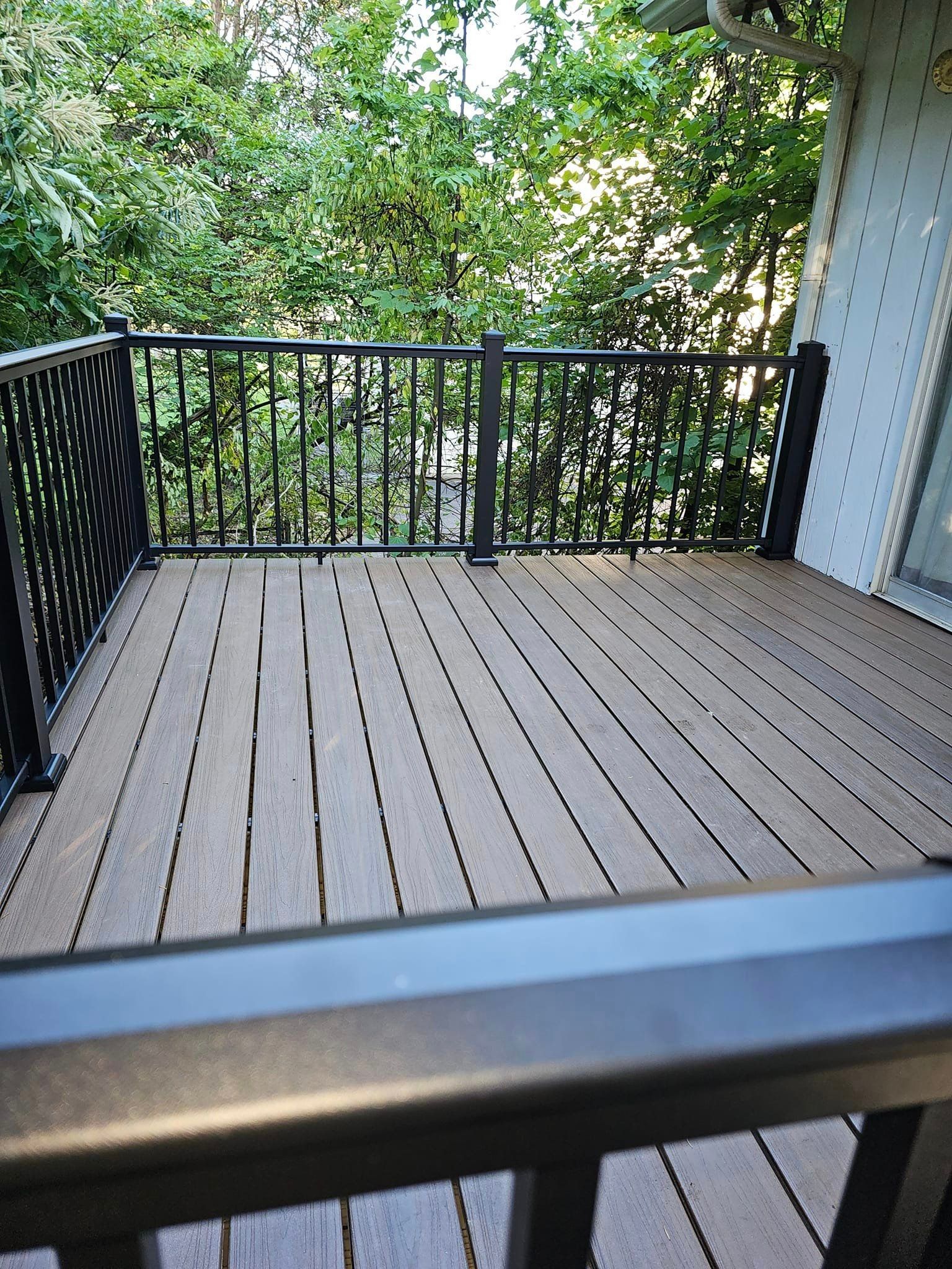 A wooden deck with a black railing and trees in the background.