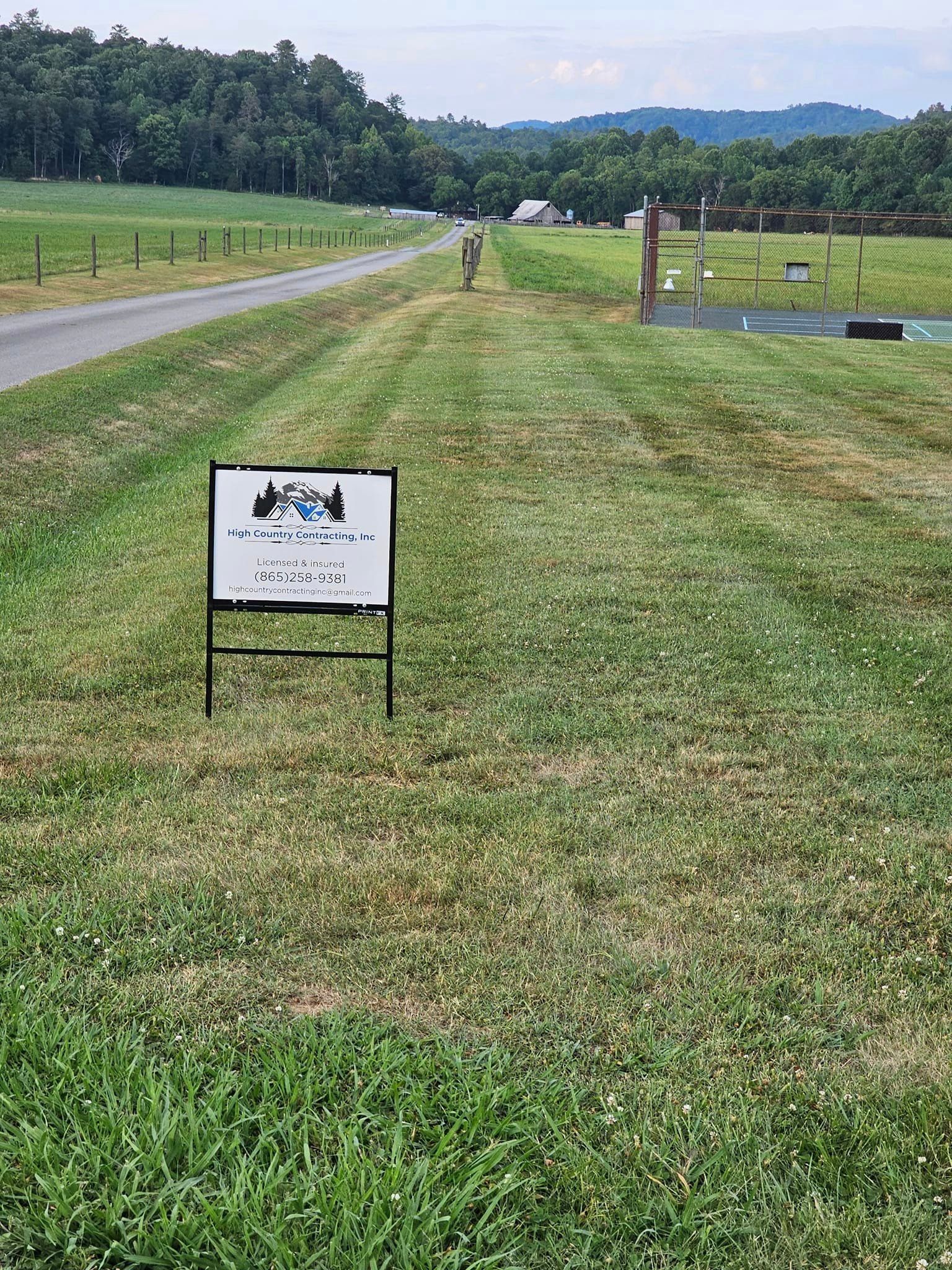 A sign is sitting in the middle of a grassy field next to a road.