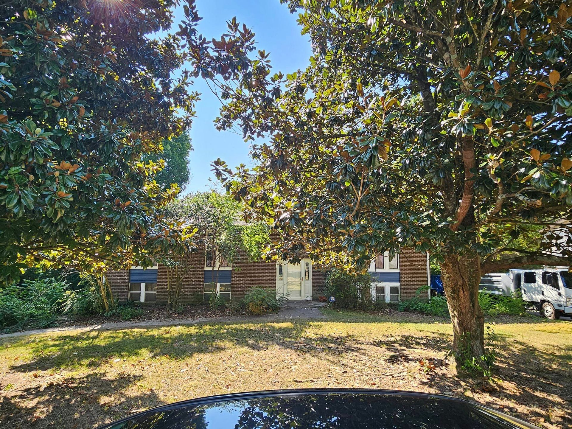 A car is parked in front of a house surrounded by trees.