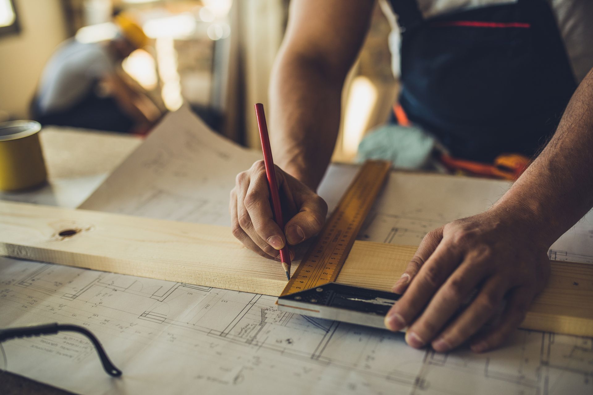A man is measuring a piece of wood with a ruler and pencil.