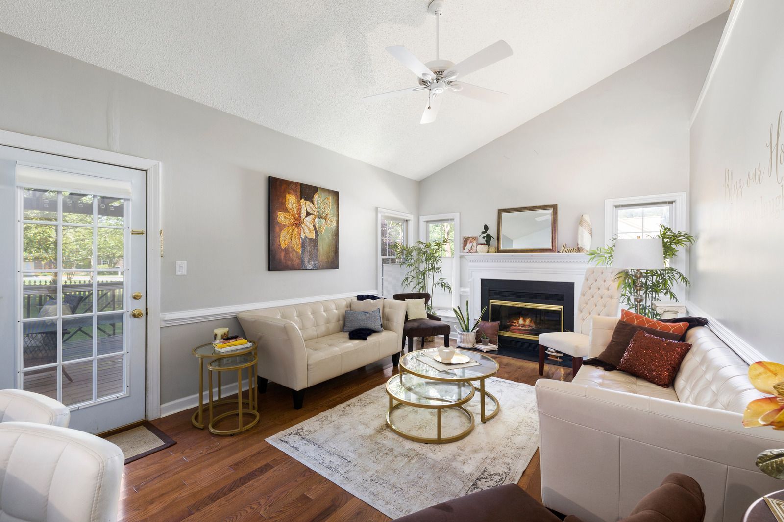 Living room with cream-colored sofas, fireplace, and glass door. Features include a rug and a gold-framed coffee table.