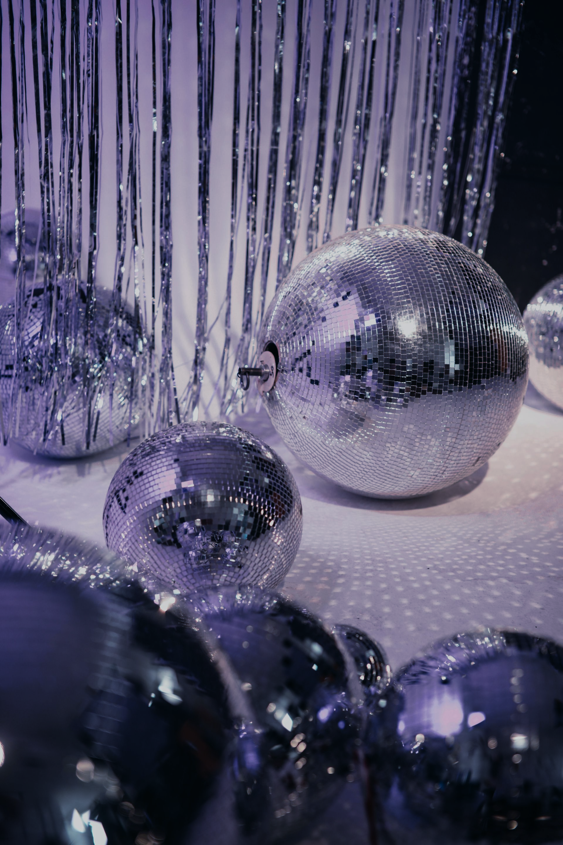 Silver disco balls on a reflective surface with silver fringe in the background.