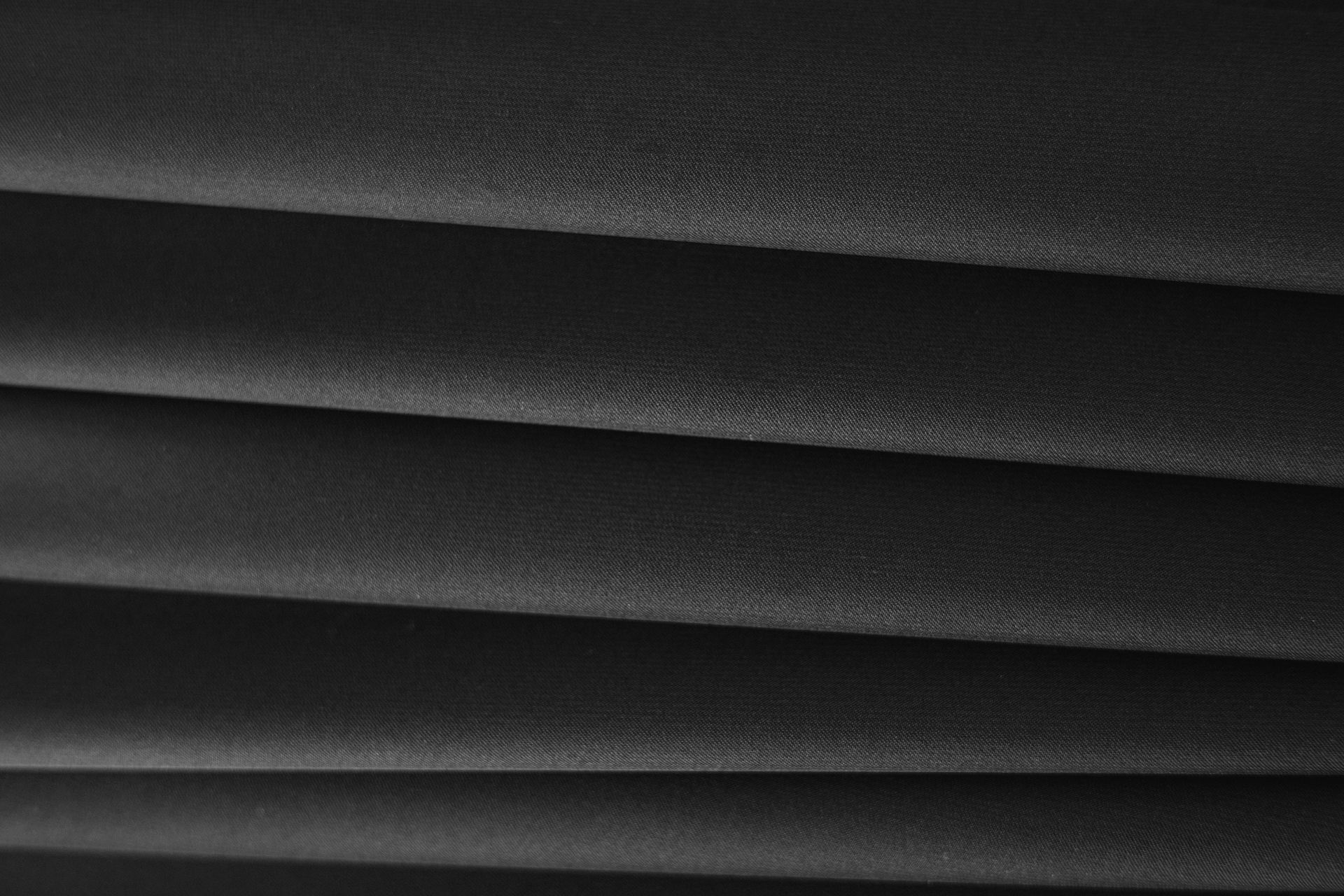 Close-up of black pleated fabric, with horizontal lines creating shadows and texture.