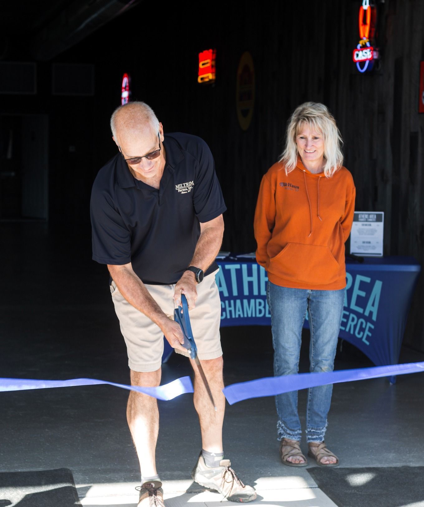 A man is cutting a blue ribbon while a woman watches