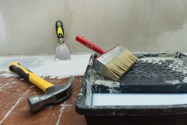 A hammer , brush , and spatula are sitting on top of a paint roller.