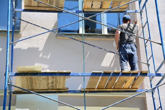 A man is standing on a scaffolding painting a building.