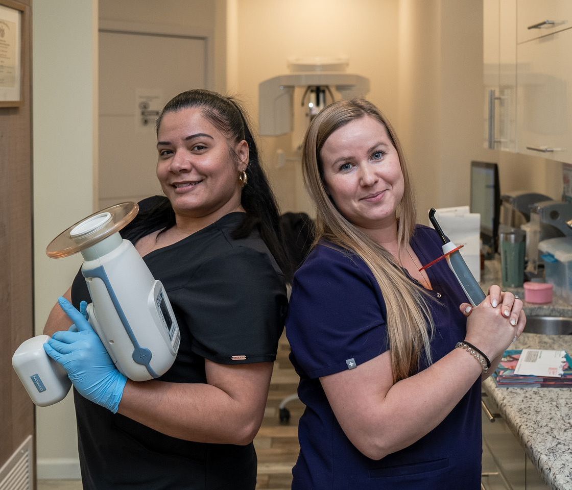 Two women wearing face masks are sitting at a desk in a dental office.