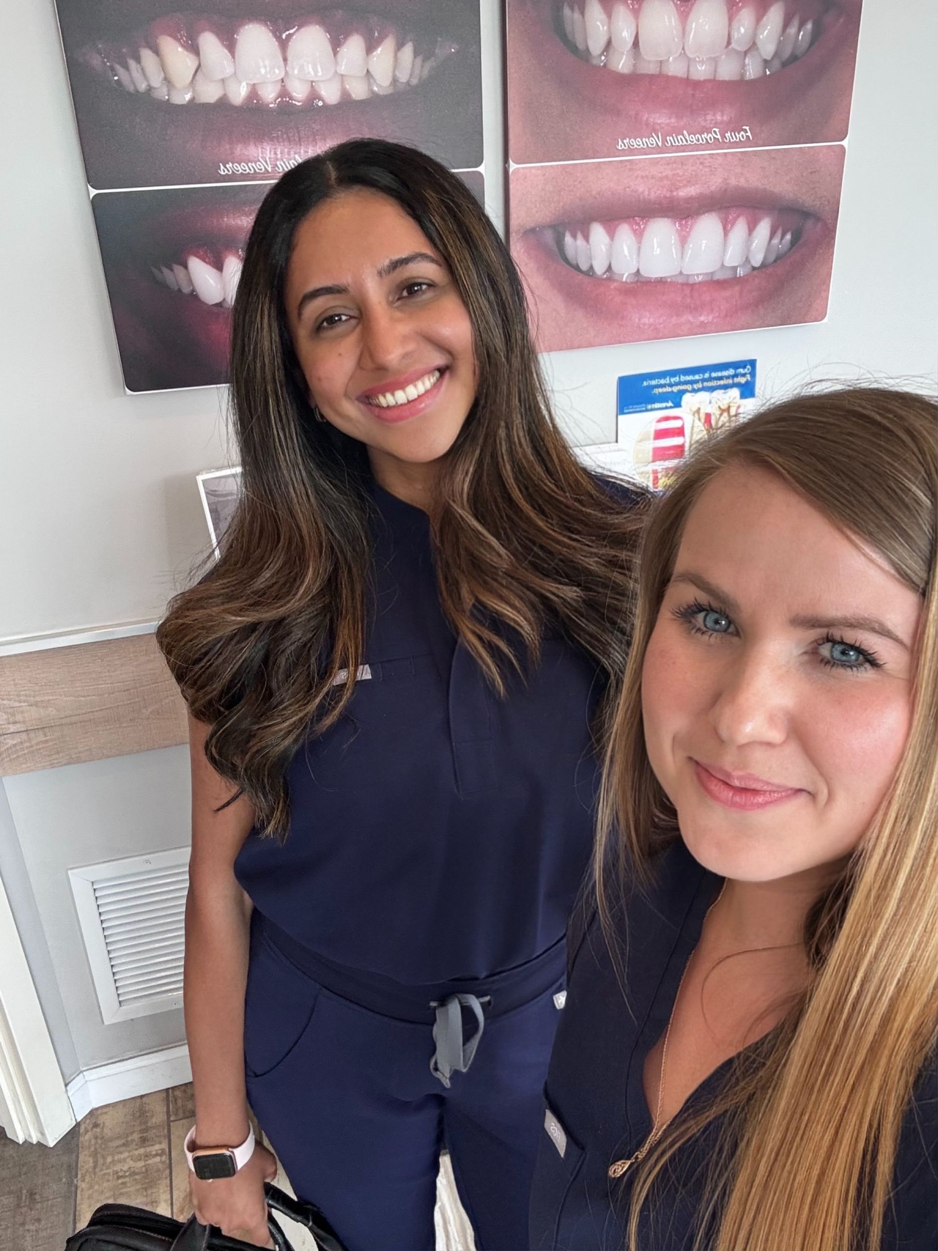 Two women are posing for a picture in front of a wall with pictures of teeth on it.
