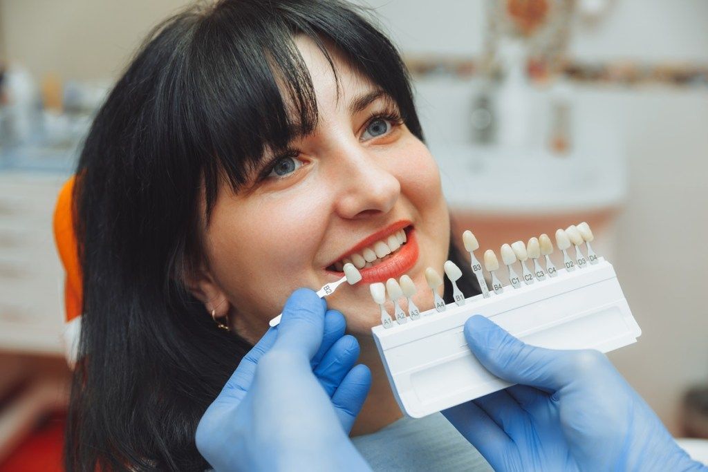 A woman is sitting in a dental chair while a dentist examines her teeth.