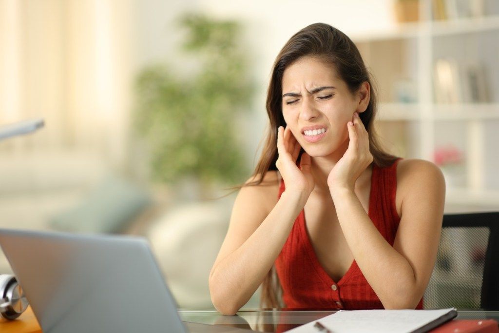A woman is sitting at a desk with a laptop and a toothache.