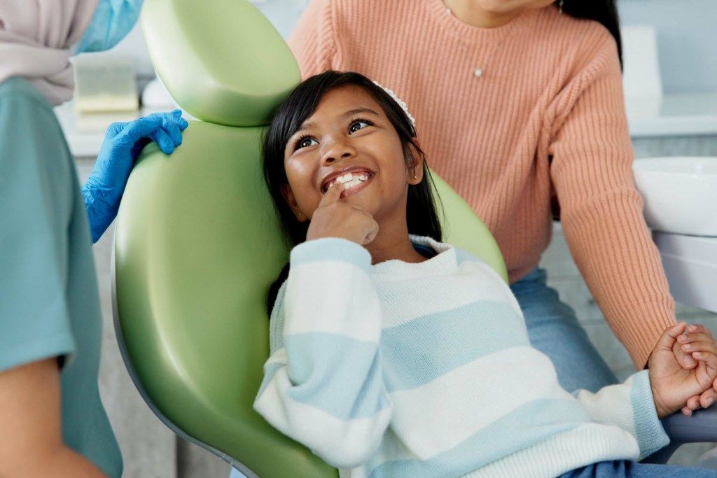 A little girl is sitting in a dental chair with her mother.