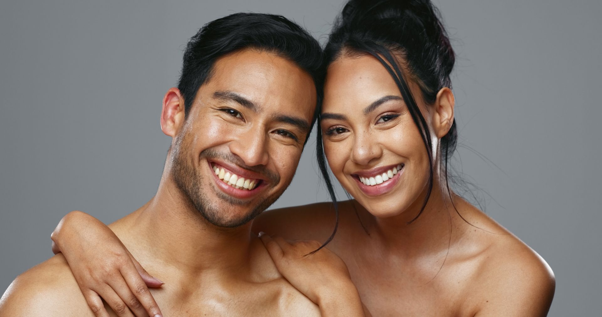 Couple smiling, embracing against gray backdrop.