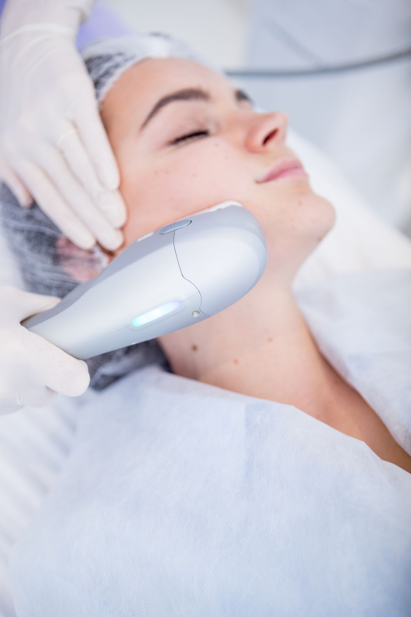 Woman undergoing facial treatment with a handheld device, in a medical setting.