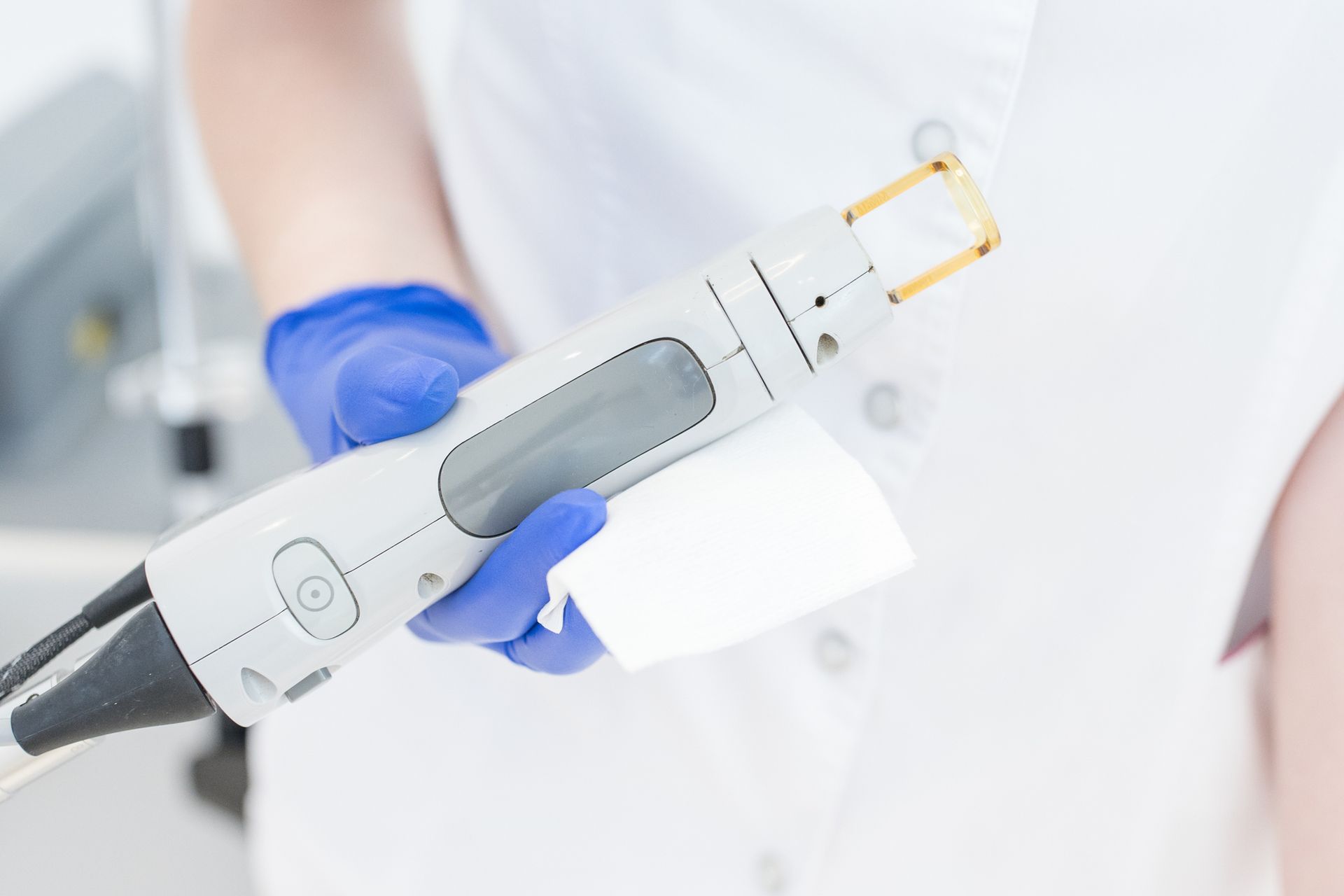 Person in blue gloves holds a laser hair removal device.
