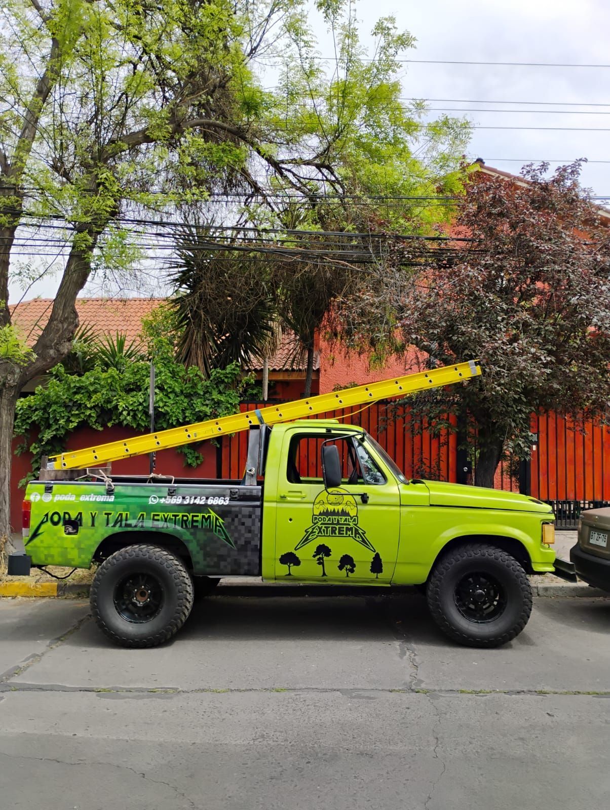Un camión verde con una escalera en la parte trasera está estacionado al costado de la carretera.