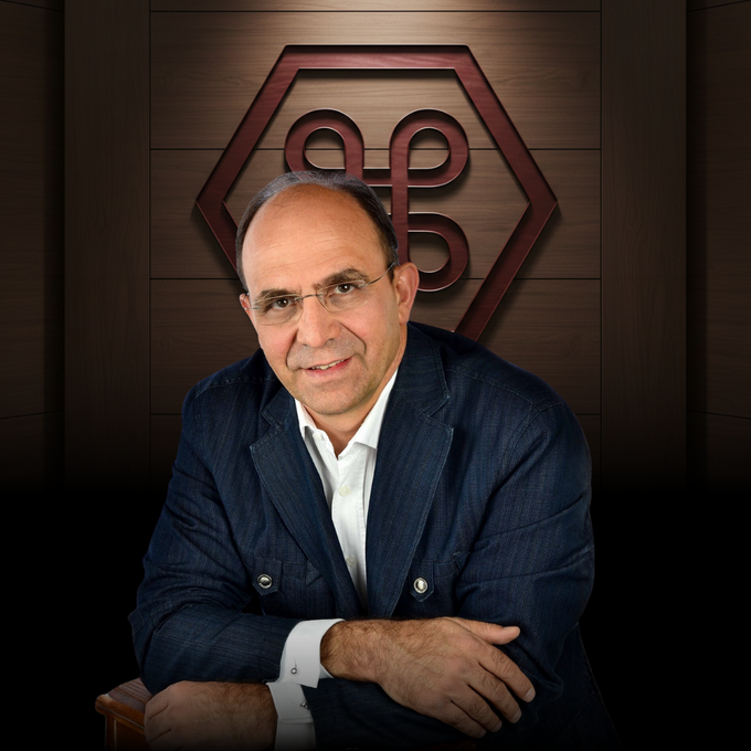 A man in a navy blazer and white shirt poses in front of a wood-paneled wall featuring a hexagonal geometric logo.