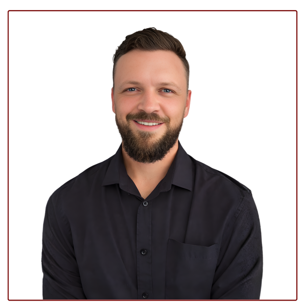 A person with a beard, wearing a black collared shirt, smiles against a plain white background.