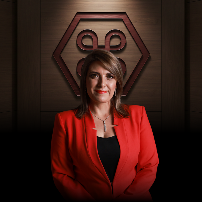 A professional woman in a red blazer stands before a wood-paneled wall featuring a hexagonal emblem.