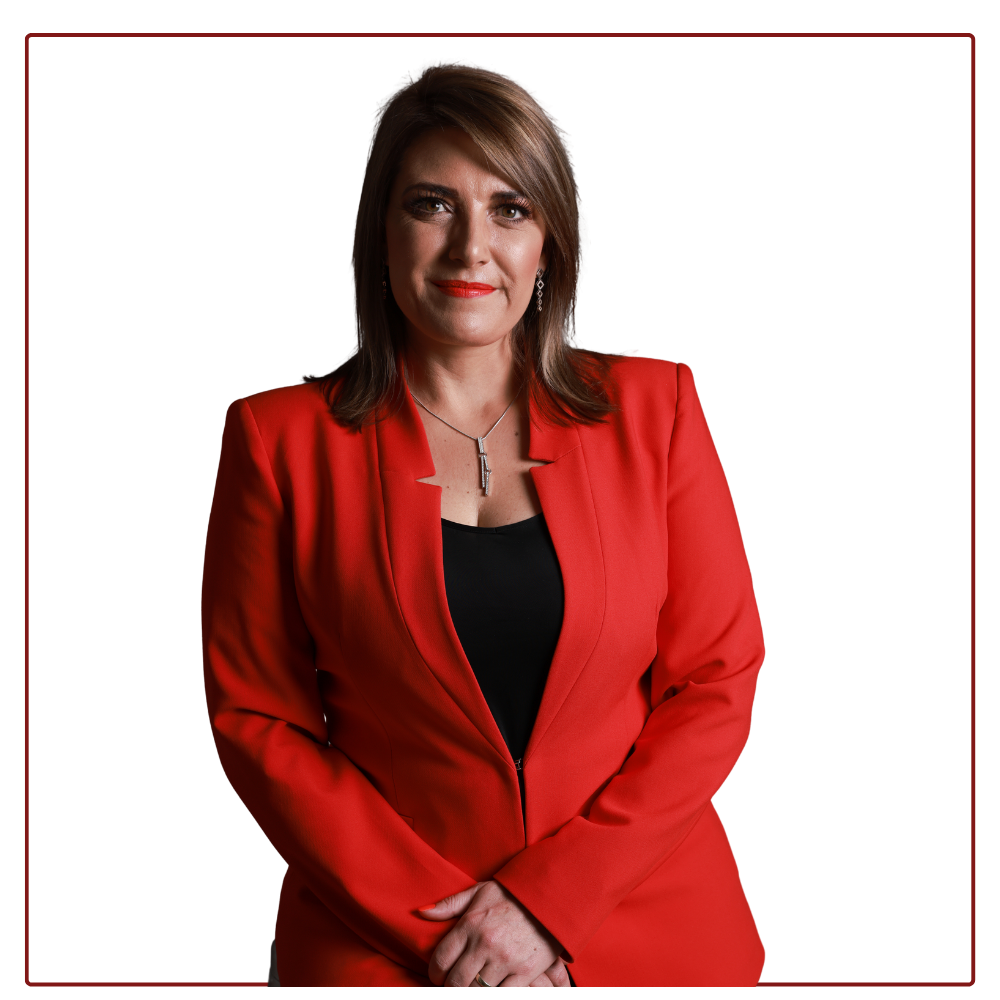 A person with shoulder-length brown hair, wearing a vibrant red blazer over a black top, poses against a white background.