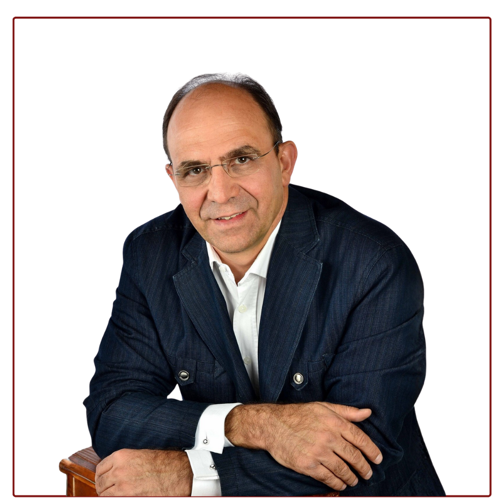 A person wearing a dark blue blazer and white shirt, resting their arms on a surface against a plain white background.