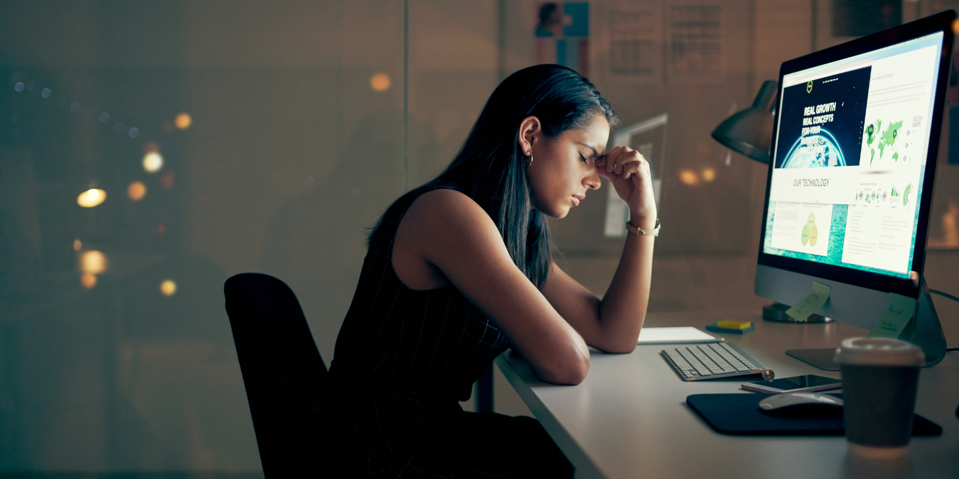 A person sits at a desk late at night, resting their head on their hand while looking at a computer screen.