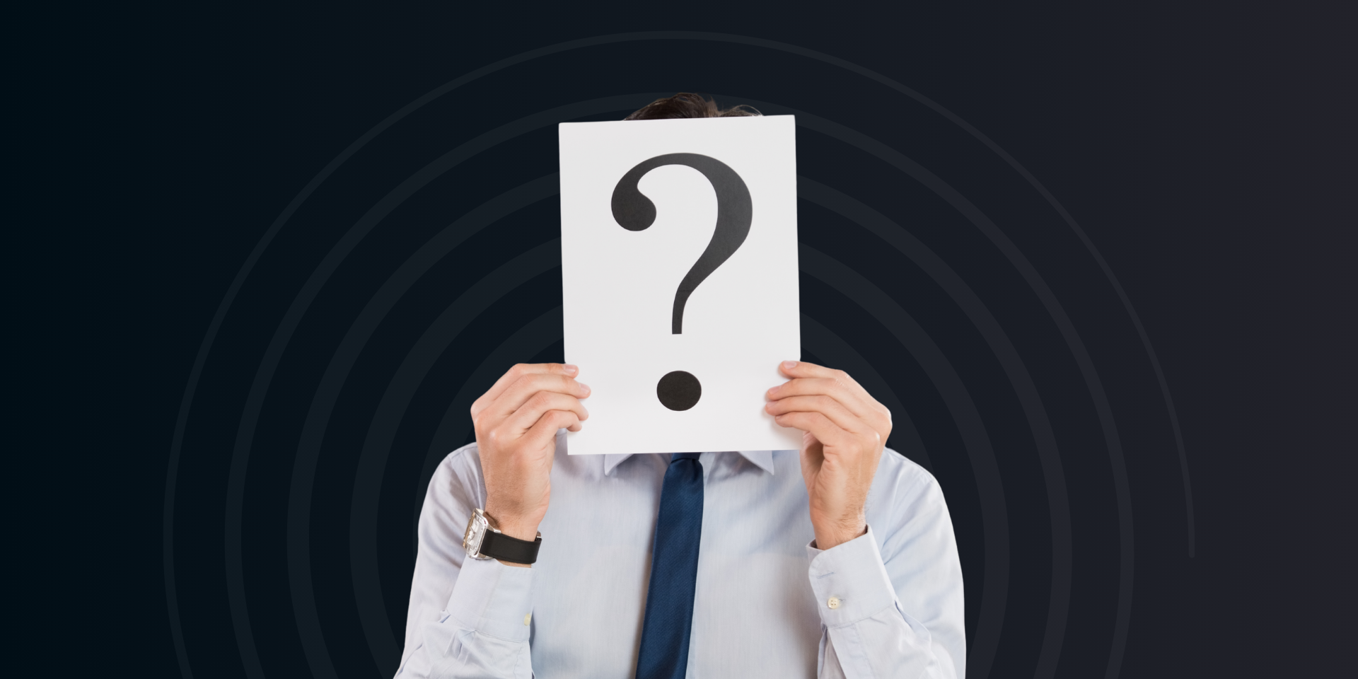 A person in a dress shirt and tie holds a white sign with a large question mark in front of their face.