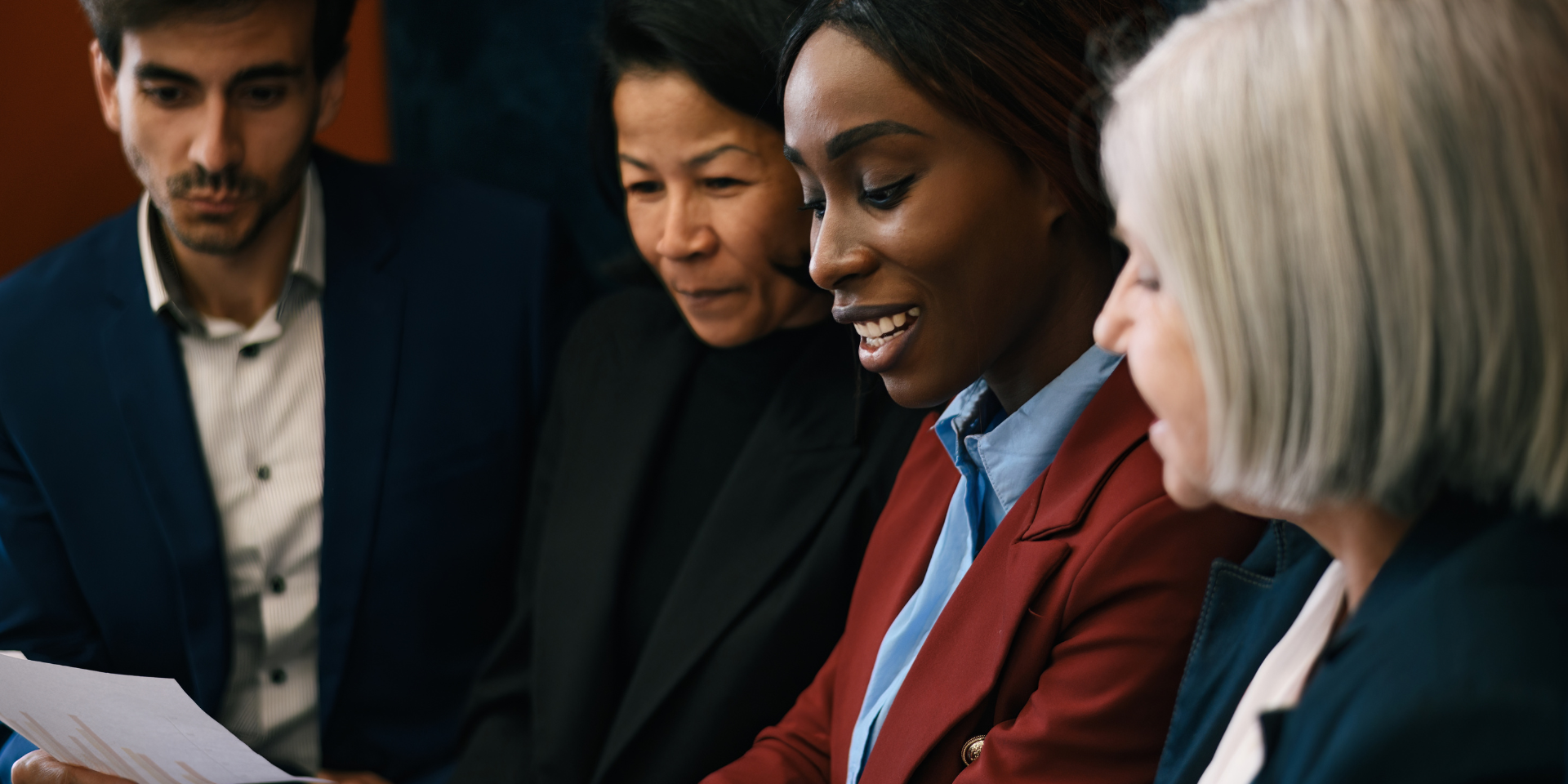 A diverse group of colleagues in business attire focused on reviewing documents together in an office setting.