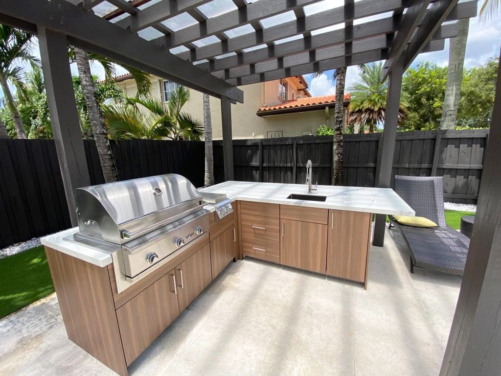 A large outdoor kitchen with a grill and sink under a pergola.