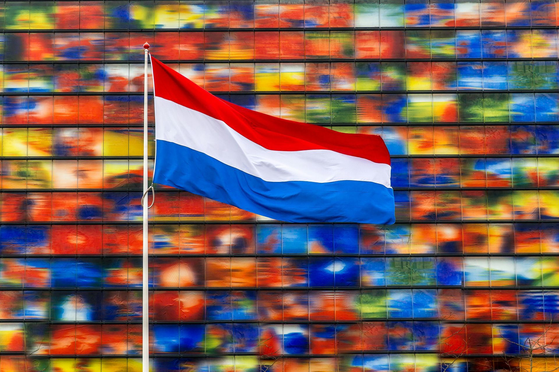 A red white and blue flag is flying in front of a colorful wall