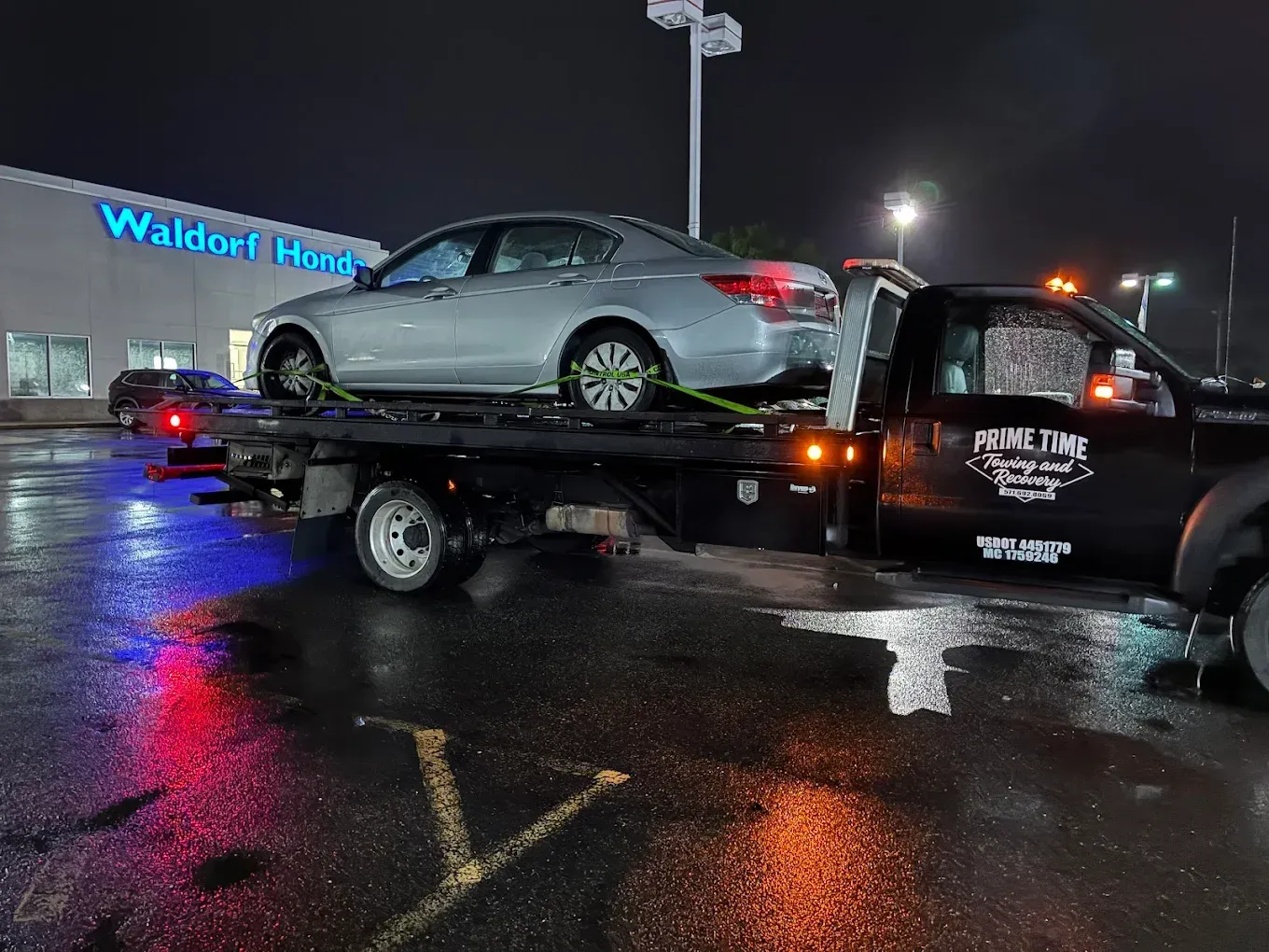 Silver sedan on a tow truck at night in a wet parking lot outside a Walmart store
