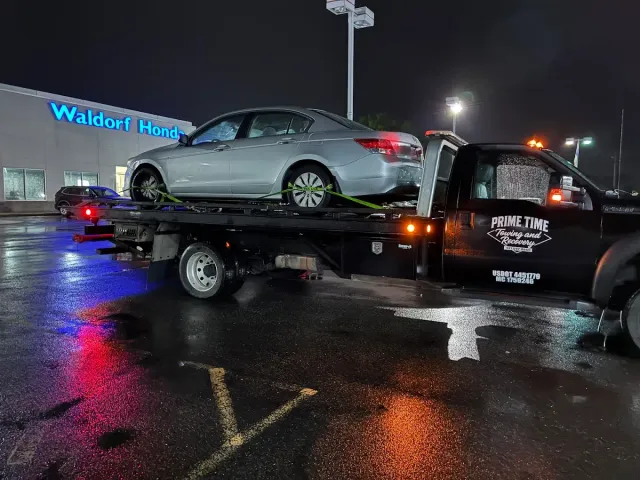 Silver sedan on a tow truck at night in a wet parking lot outside a Walmart store