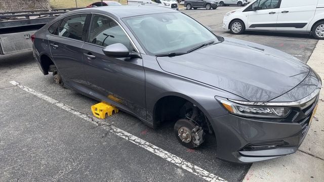 Gray sedan parked in a lot with a wheel removed and a yellow wheel chock underneath