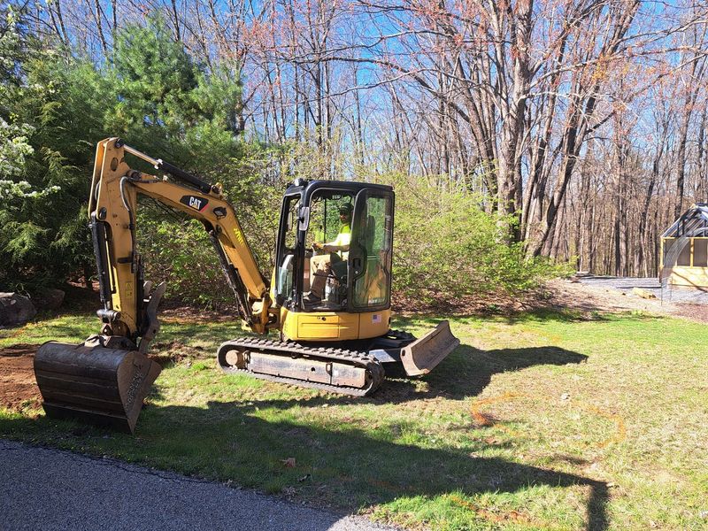 A man is driving a yellow excavator in a grassy field.