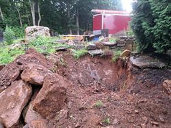 A pile of rocks and dirt in a yard with a red trailer in the background.