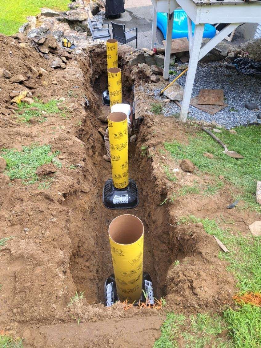 A row of yellow pipes are being installed in a hole in the ground.
