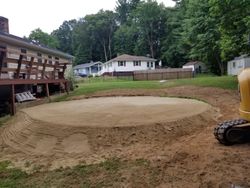 A bulldozer is moving dirt in a backyard in front of a house.
