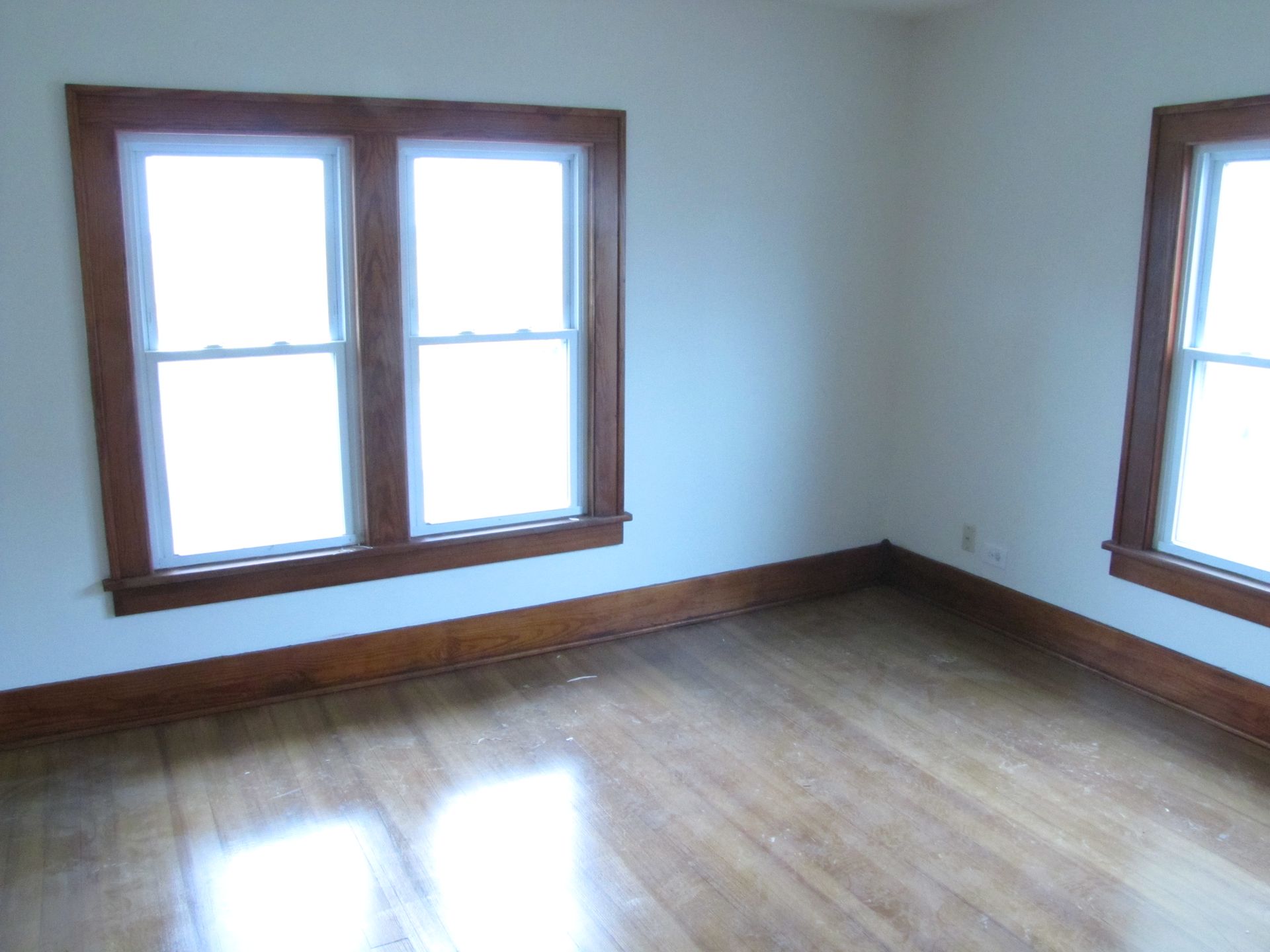 An empty room with two windows and a wooden floor
