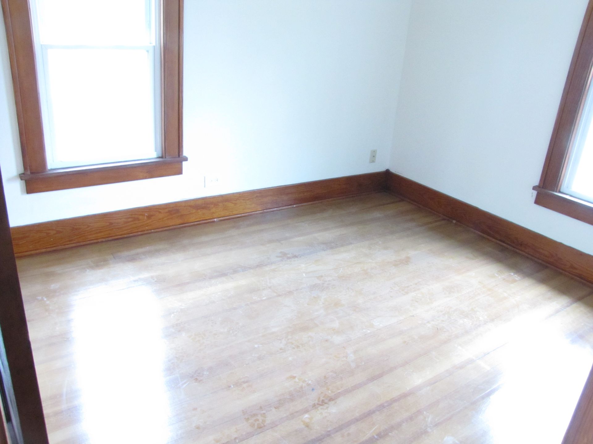 An empty room with hardwood floors and two windows