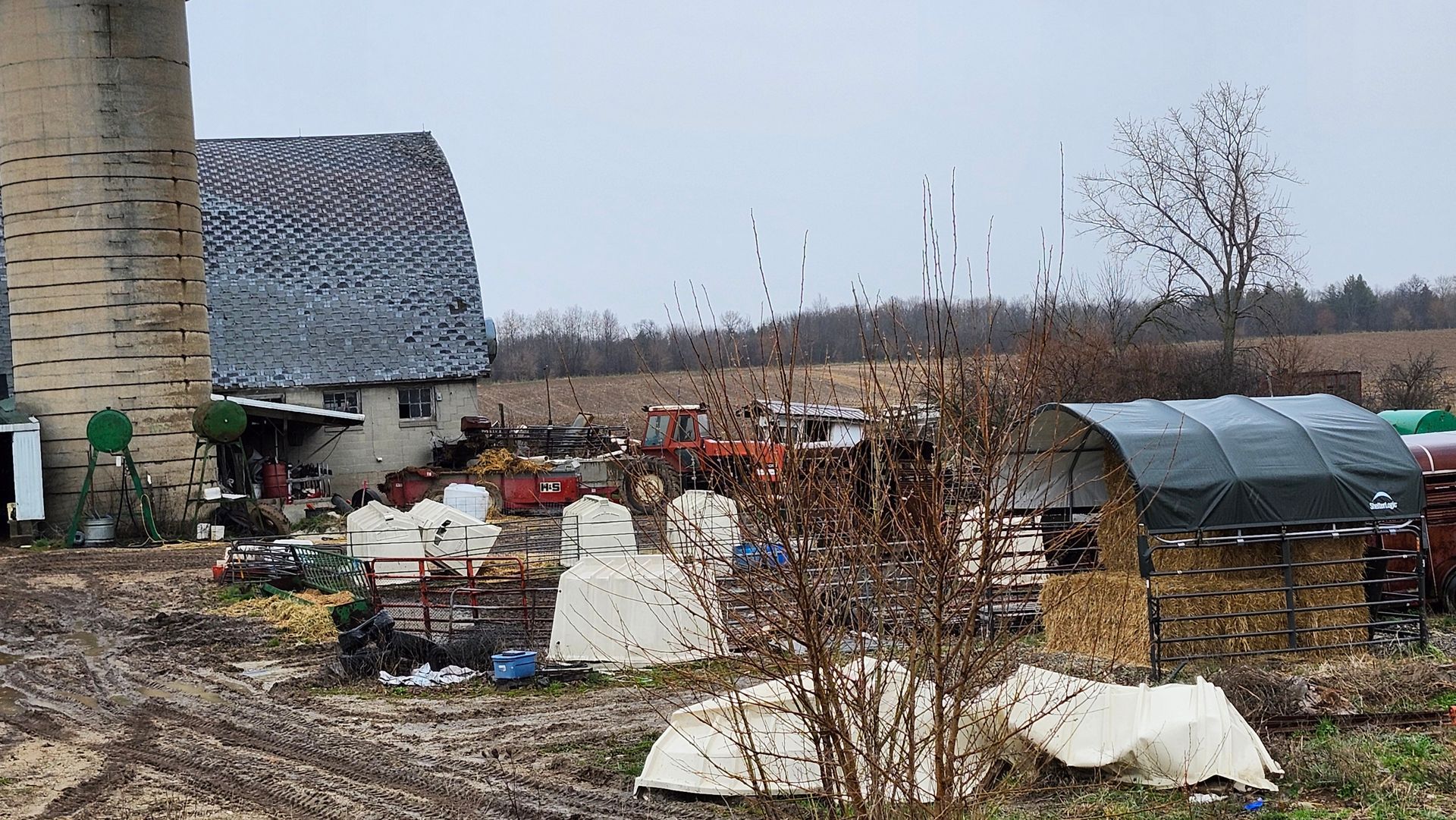A farm with a silo and a greenhouse in the background.