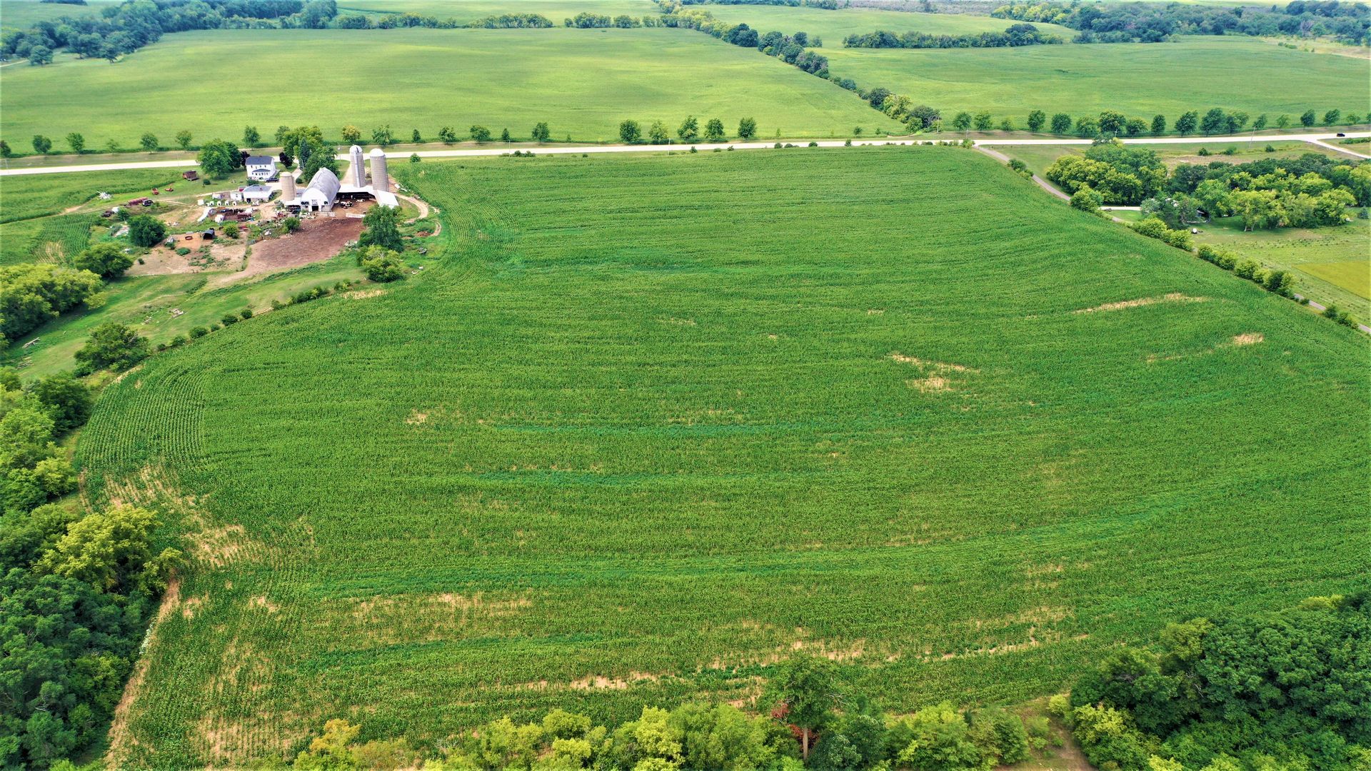 An aerial view of a large green field with a farm in the background.