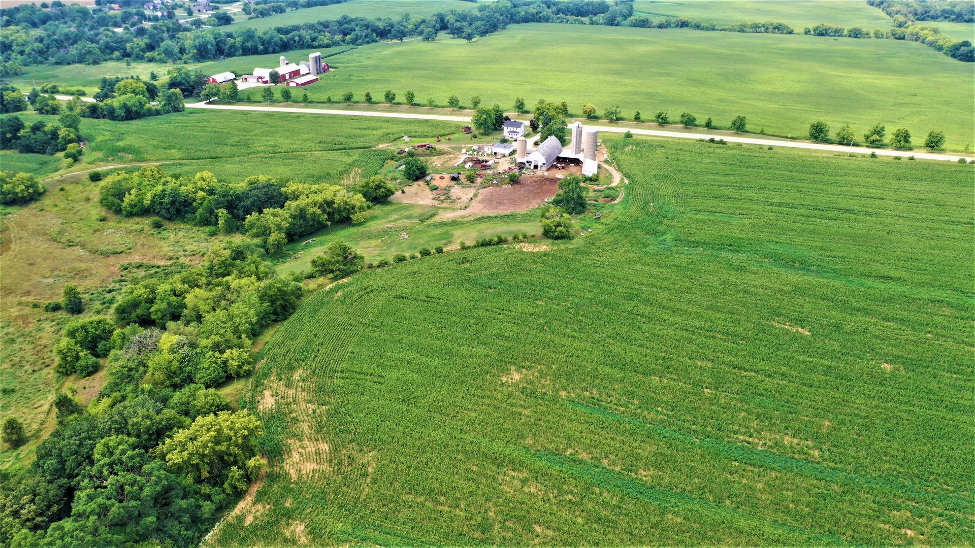 An aerial view of a large green field with a farm in the background.