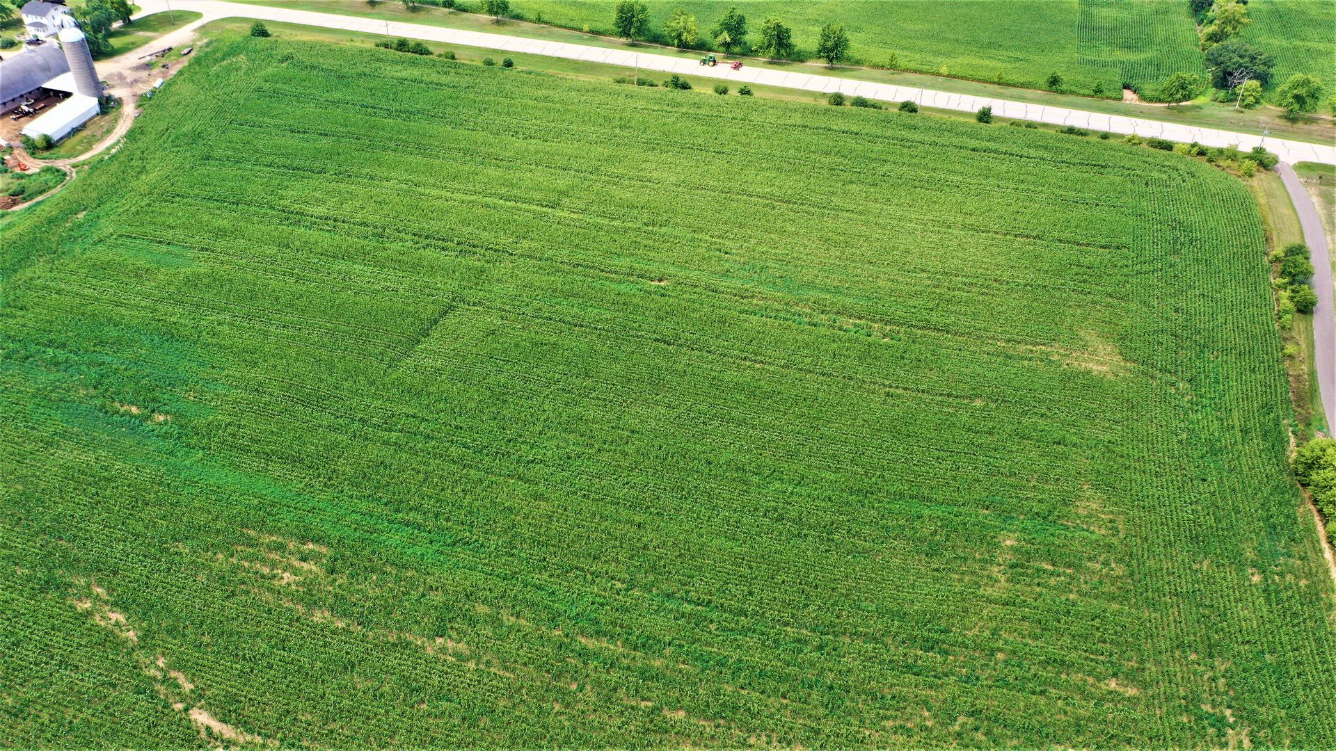 An aerial view of a large green field with a road going through it.