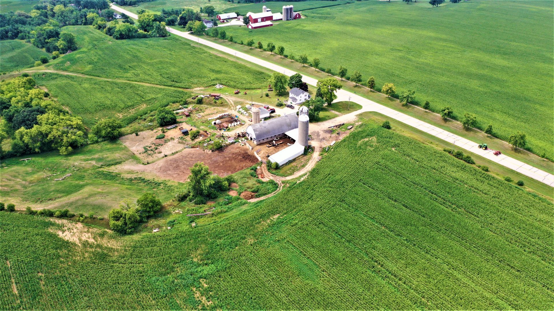 An aerial view of a farm with a silo and a road.