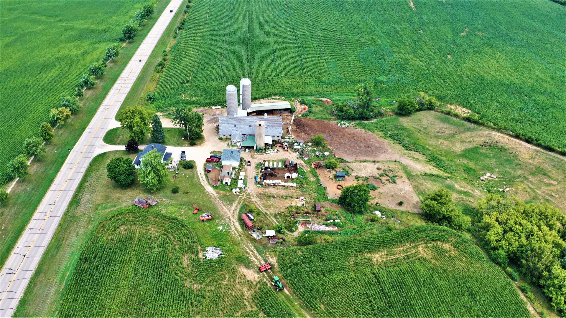 An aerial view of a farm surrounded by green fields and a road.